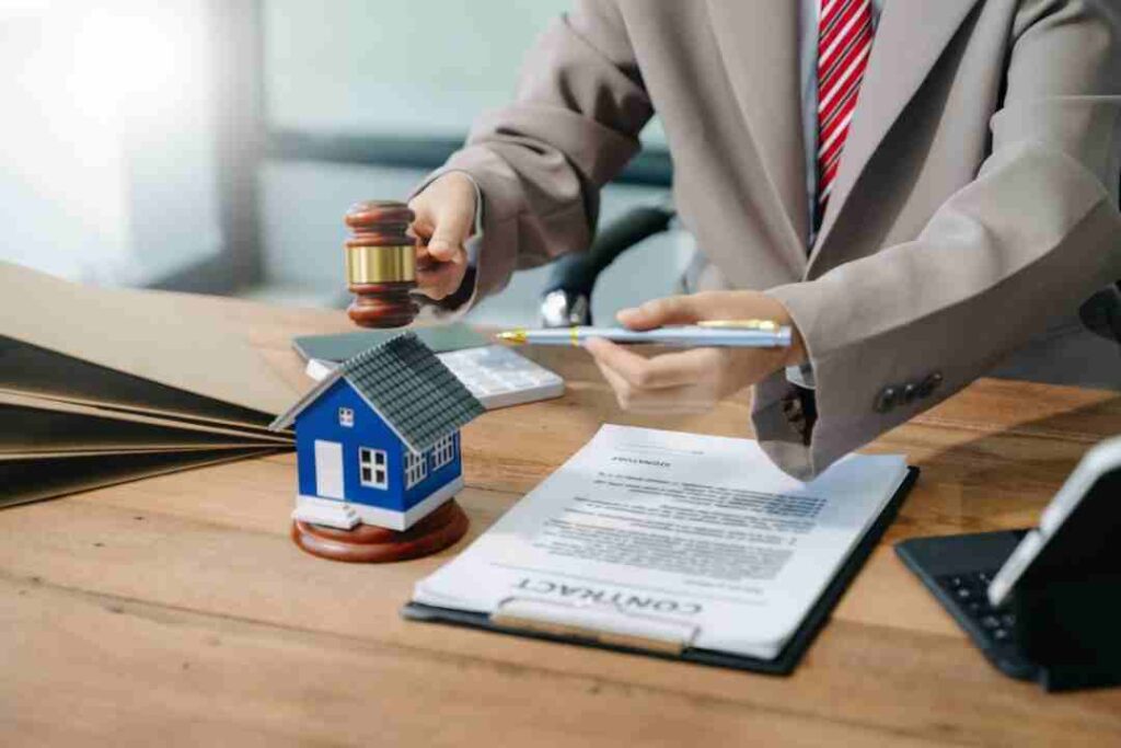 Lawyer holding a gavel and pen near a contract and a model house.